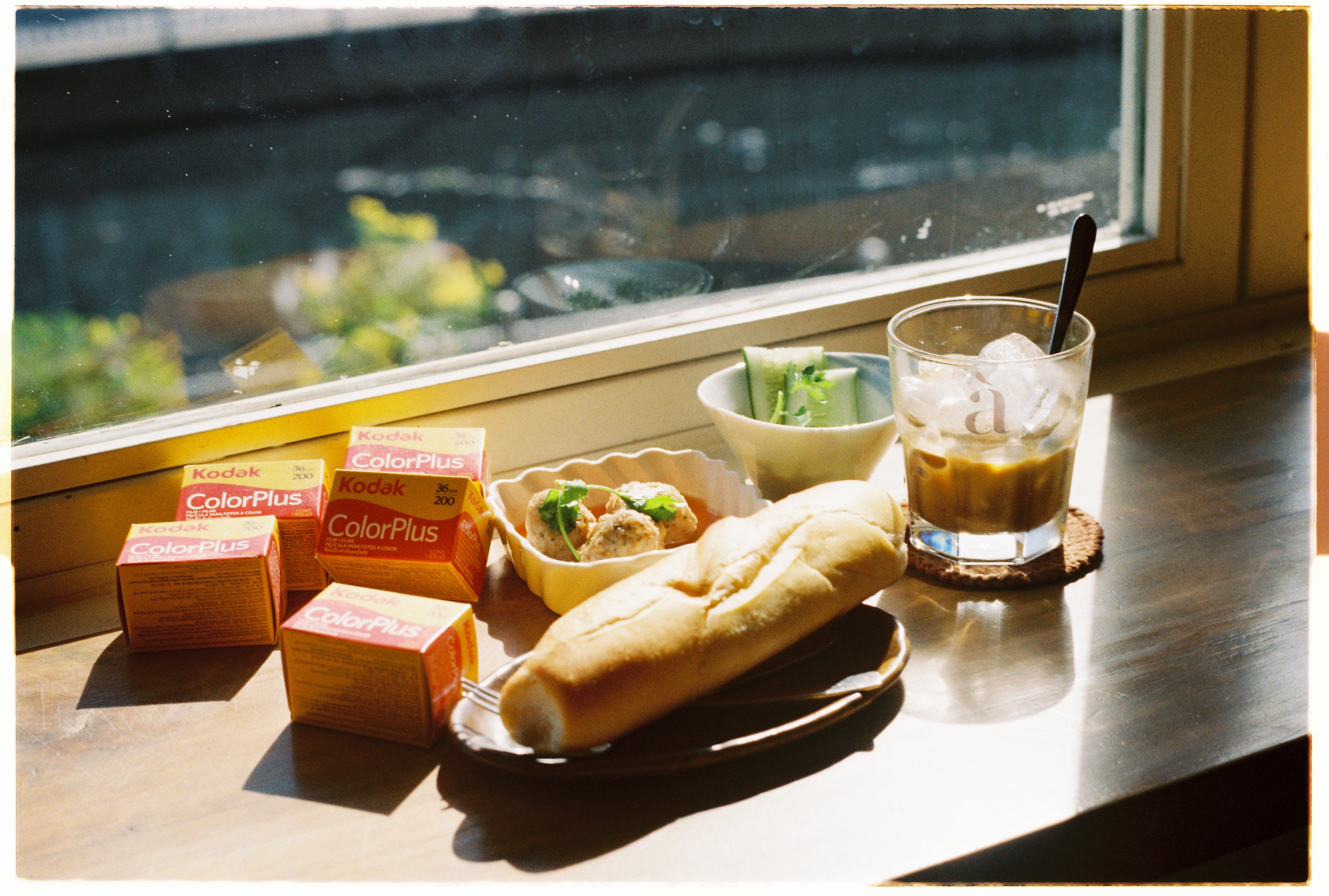 A cozy windowsill breakfast with iced coffee, bread, and Kodak film boxes.