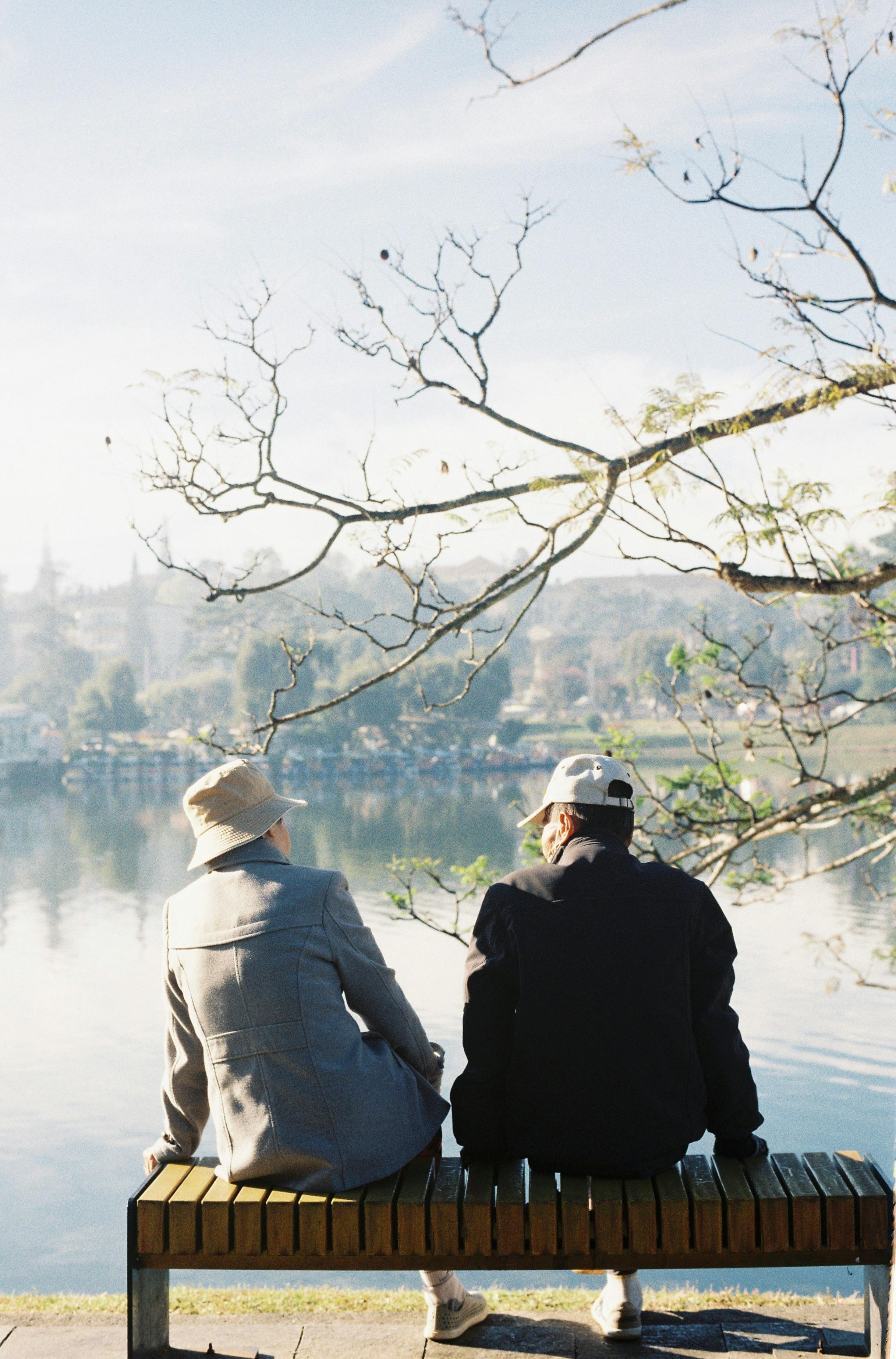 An older couple enjoying a peaceful moment by the lake under a clear sky, captured in a tranquil setting.