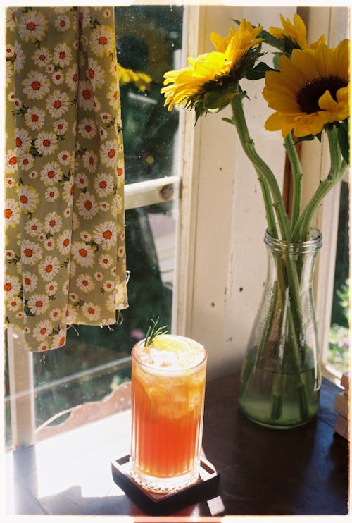 A glass of iced tea sits on a table next to sunflowers