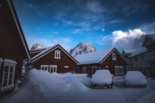 Free Scenic view of traditional red wooden houses amid snow, surrounded by mountains in winter. Stock Photo