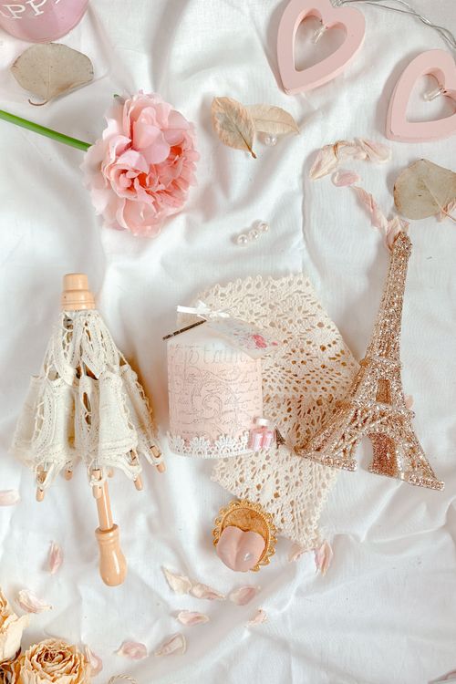 Free Elegant flat lay featuring a miniature Eiffel Tower, lace accessories, and pink florals on a white background. Stock Photo