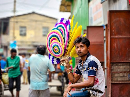 A man sitting on a street with a colorful feather
