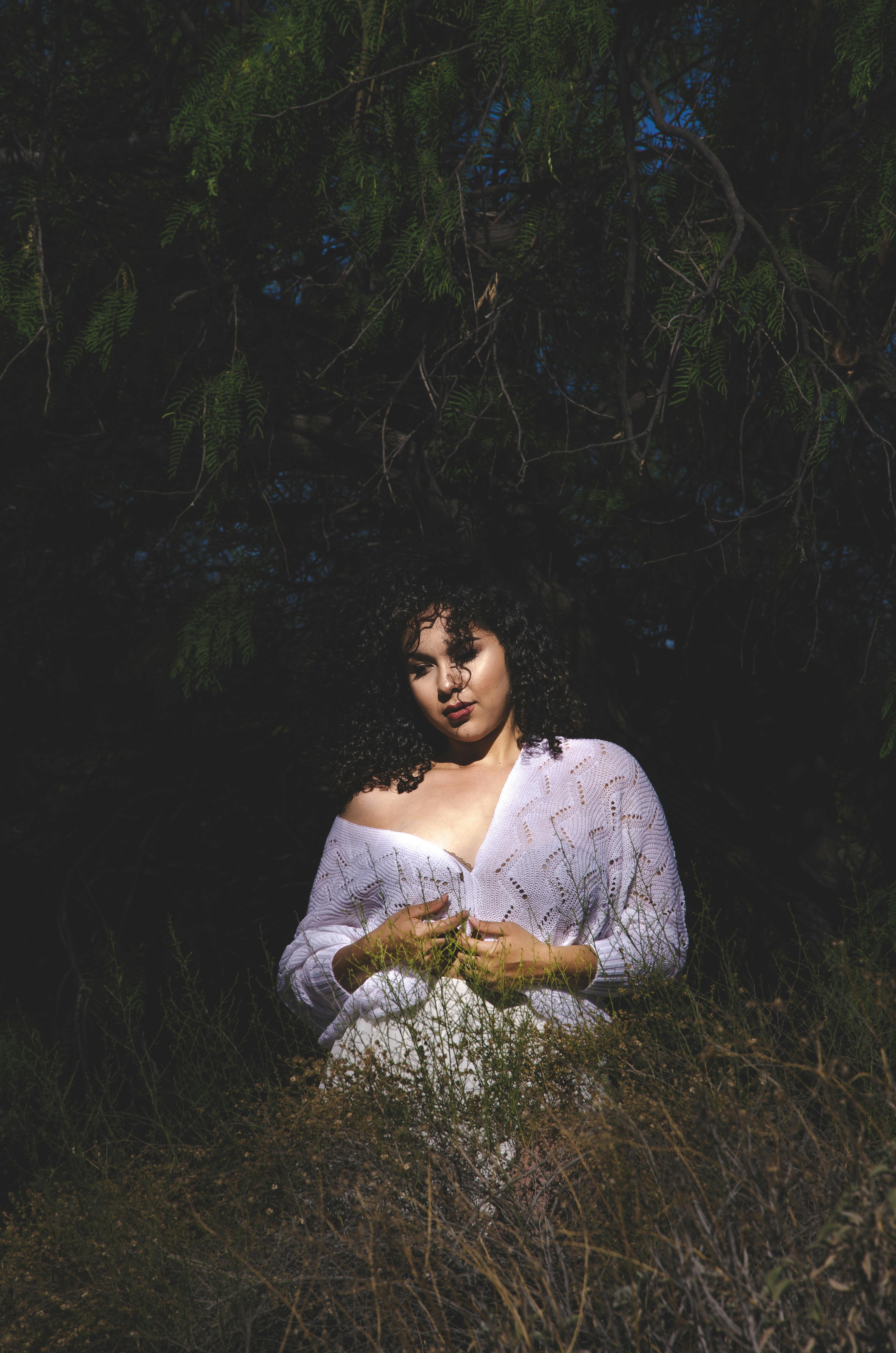 夜晚，一个女人穿着白衣，站在昏暗的自然环境中，四周树木环绕，枝叶茂密