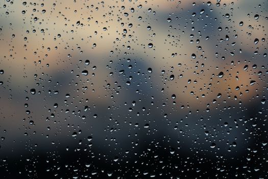 Close-up of raindrops on a window with a blurred evening sky in the background.