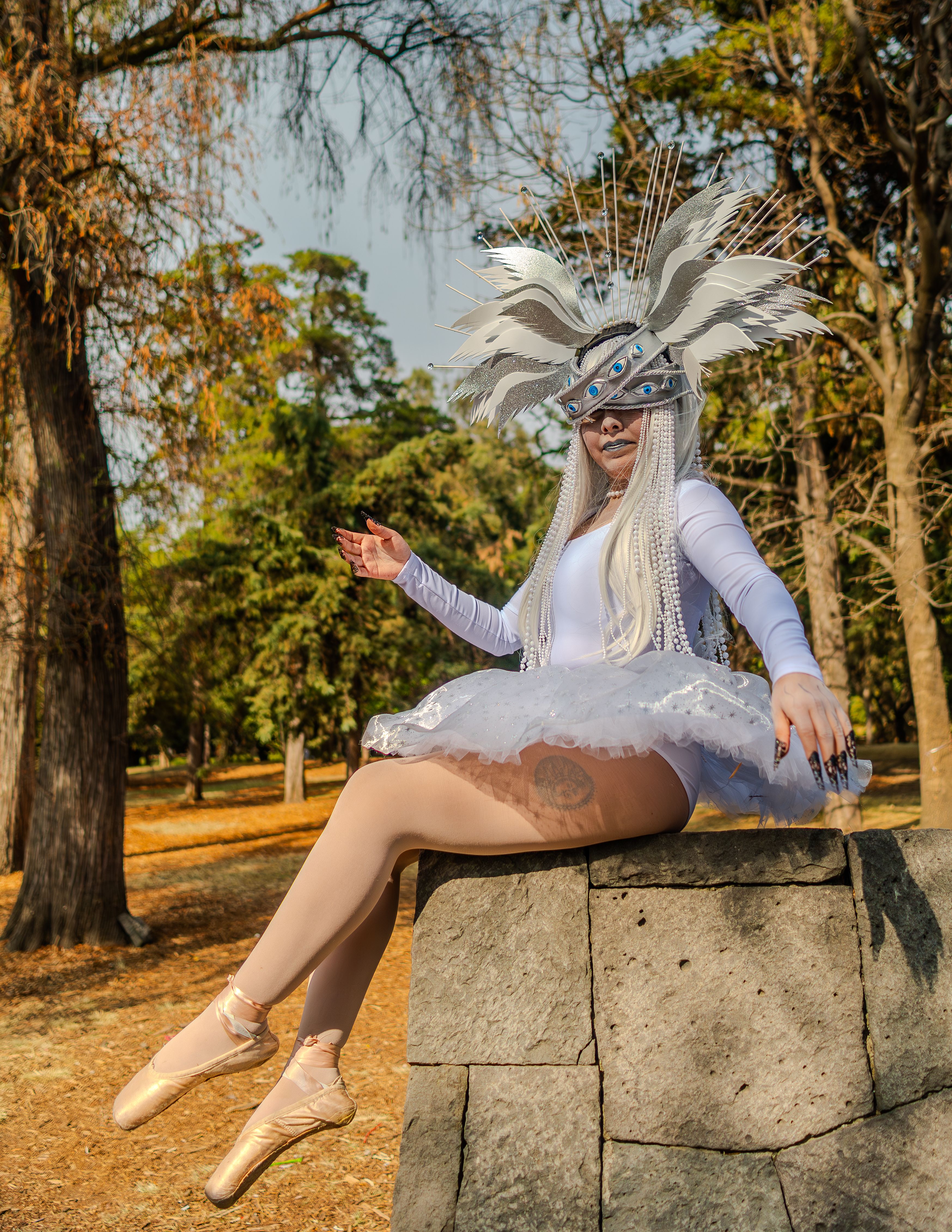 A whimsical ballerina with a unique headdress posing in an autumn park.