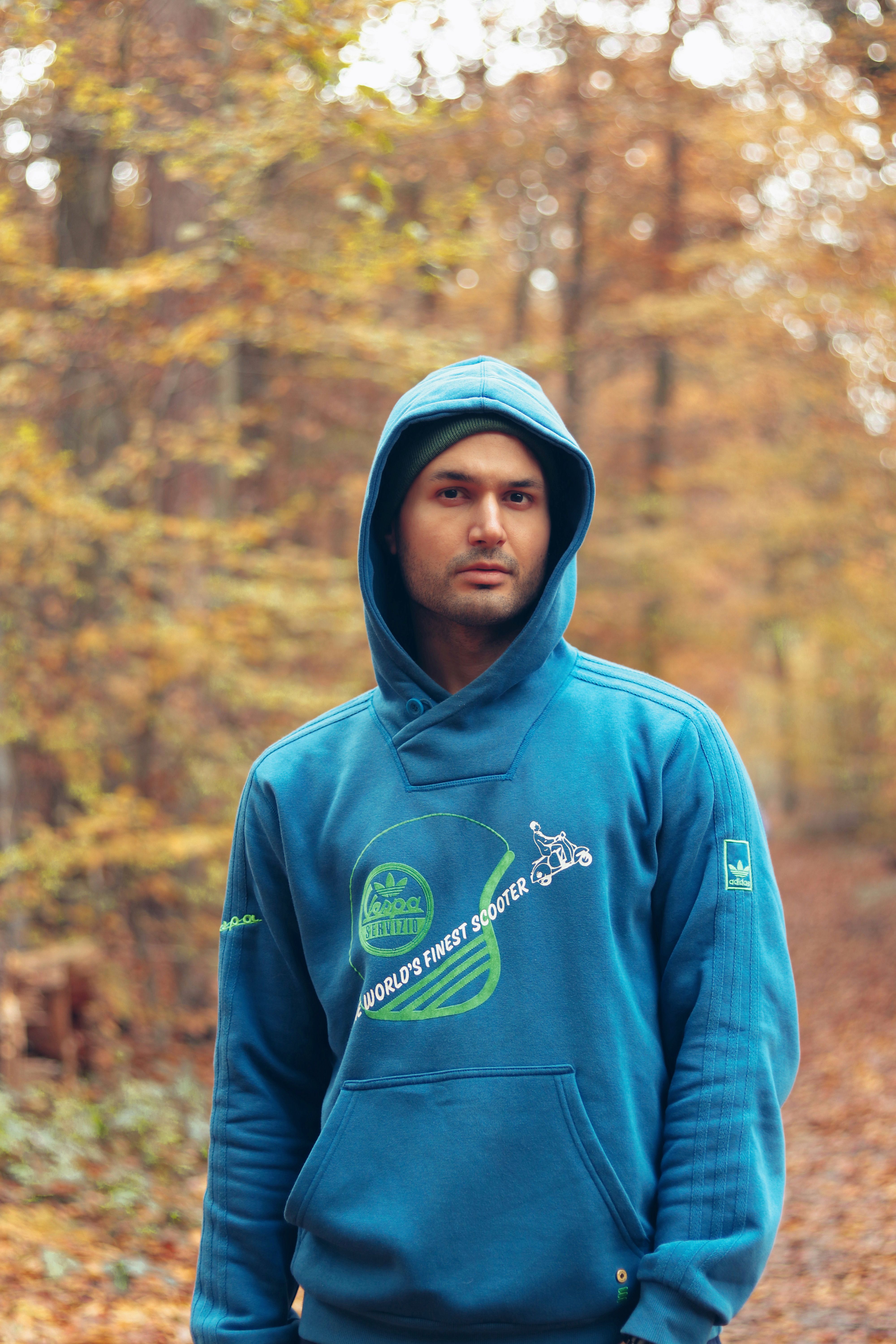 Man in blue hoodie standing in autumn forest, showcasing fall fashion.