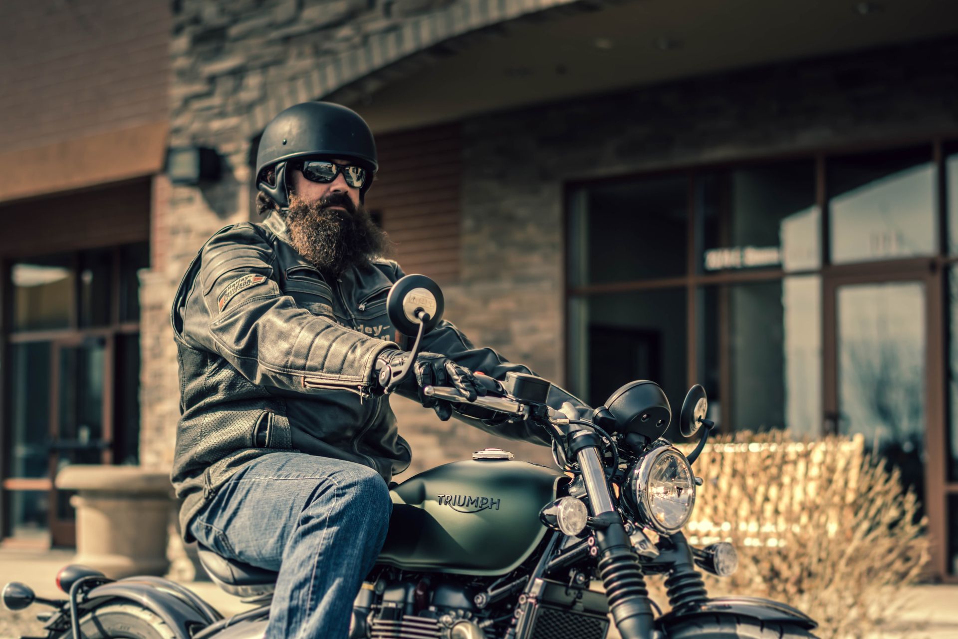 A bearded man rides a classic motorcycle in an urban environment, exuding a cool and rugged style.