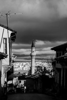 Monochrome cityscape featuring a historic Turkish minaret under dramatic clouds.