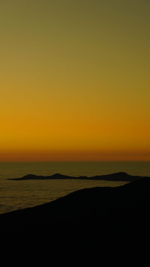 Free A scenic coastal sunset featuring silhouettes of hills against a vibrant yellow sky. Stock Photo