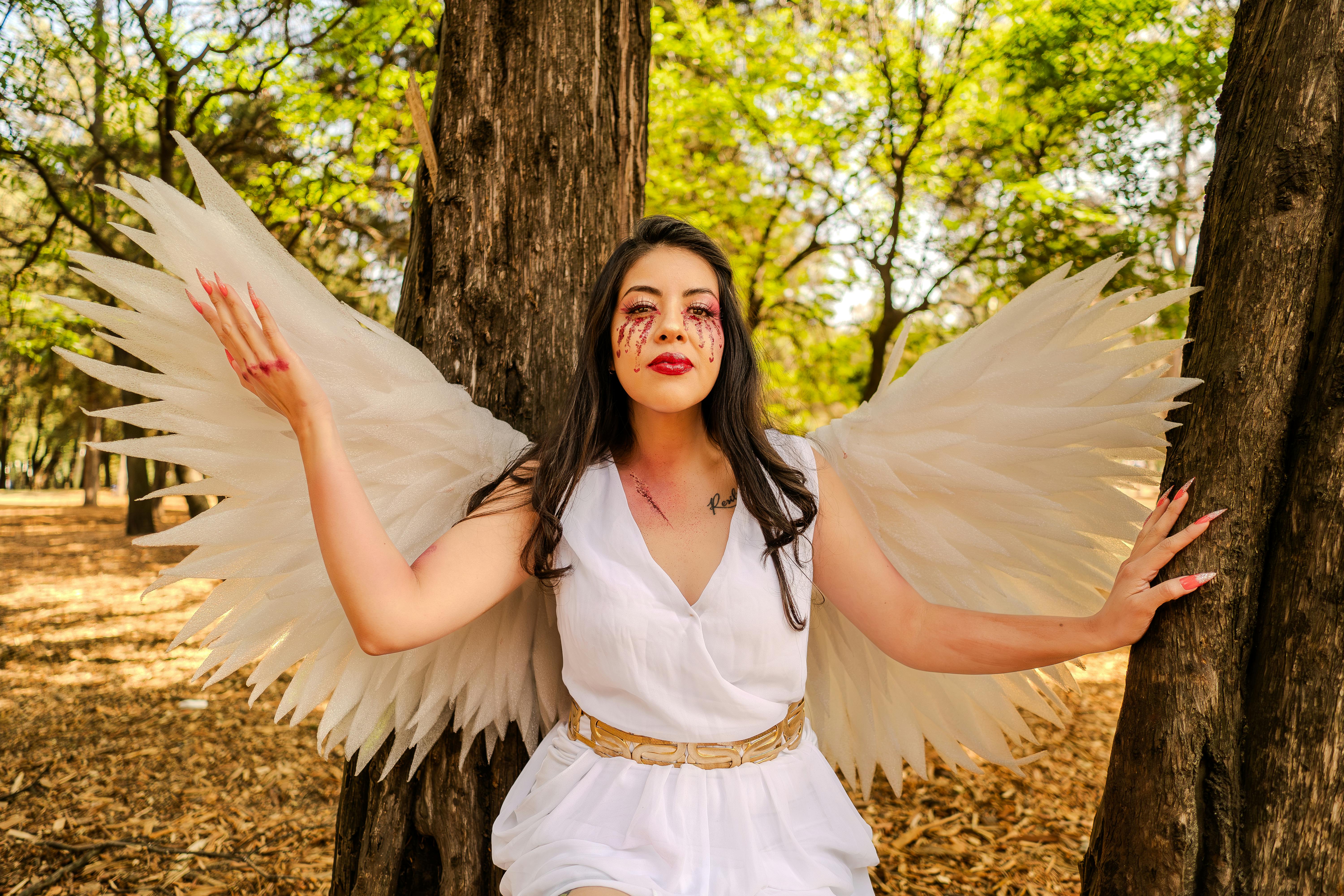 A woman dressed as an angel with wings, posing gracefully in a sunlit park. A whimsical and serene portrait.