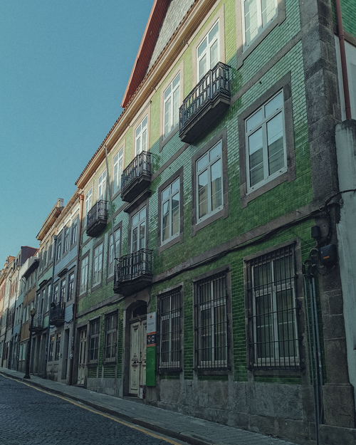 Free A classic green brick building with balconies lining a quiet city street under bright daylight. Stock Photo