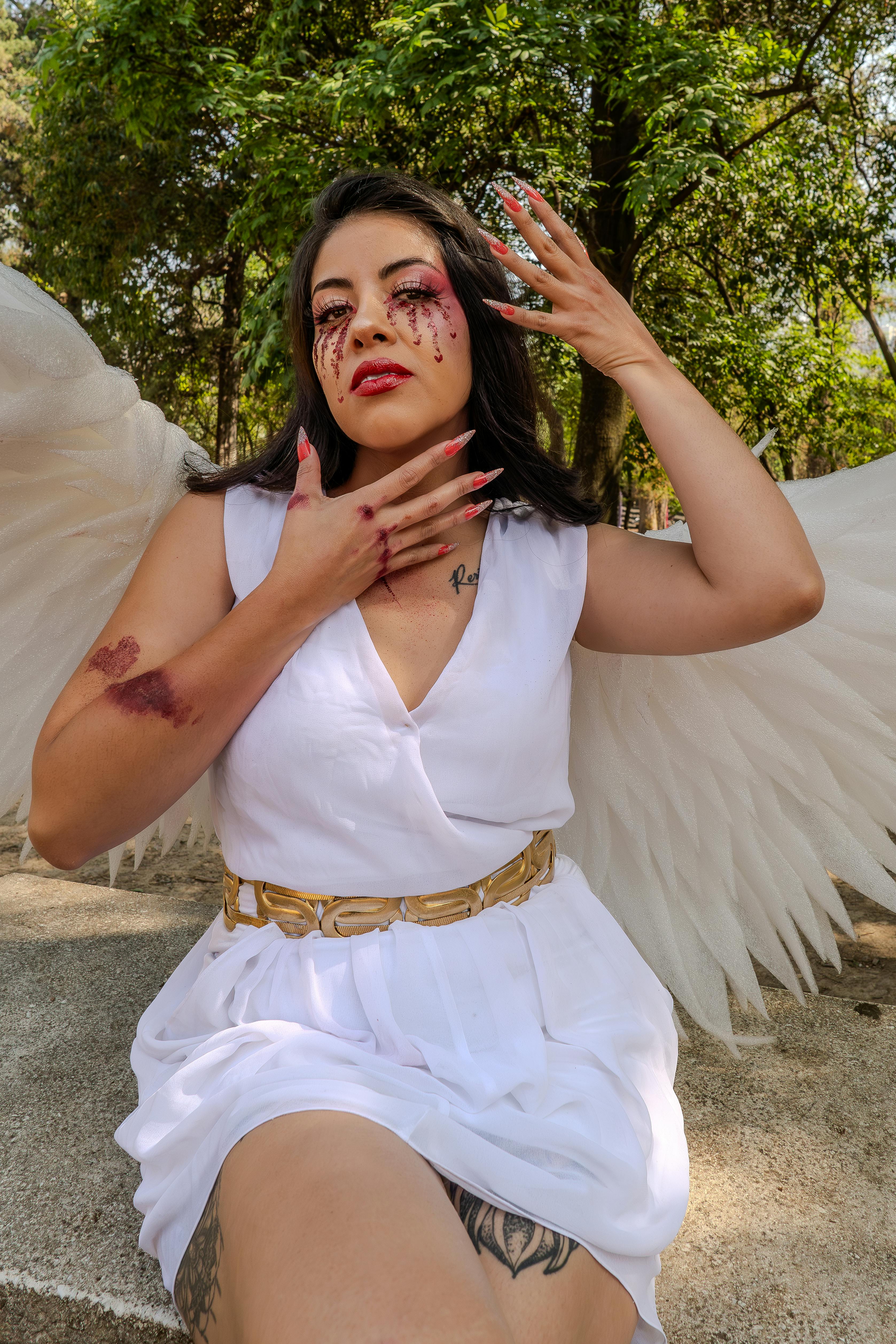 Conceptual outdoor portrait of a woman with angel wings and dramatic makeup, evoking strong emotions.