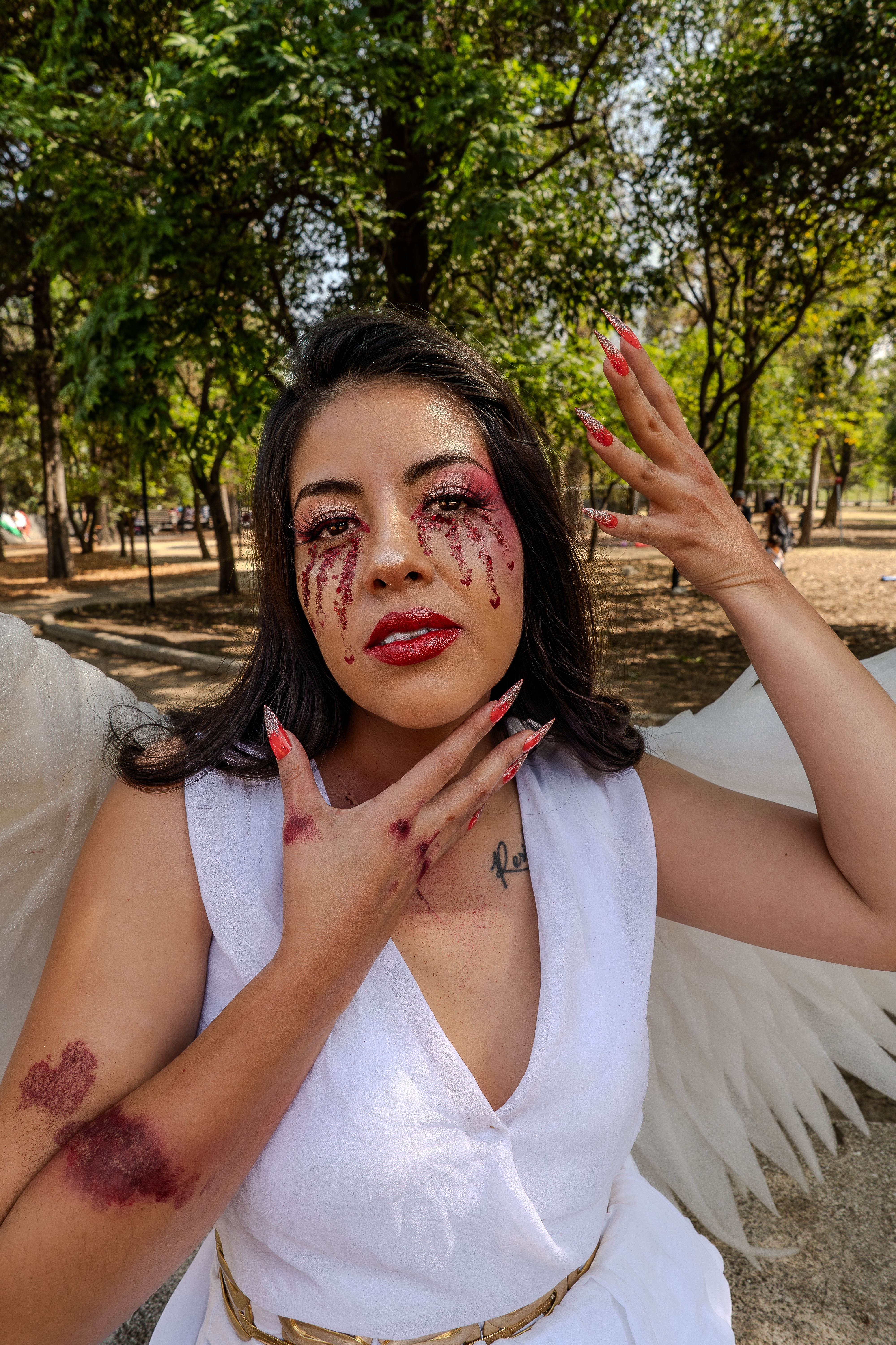 Striking outdoor portrait of a woman with angel wings and creative makeup, evoking a dreamy conceptual style.