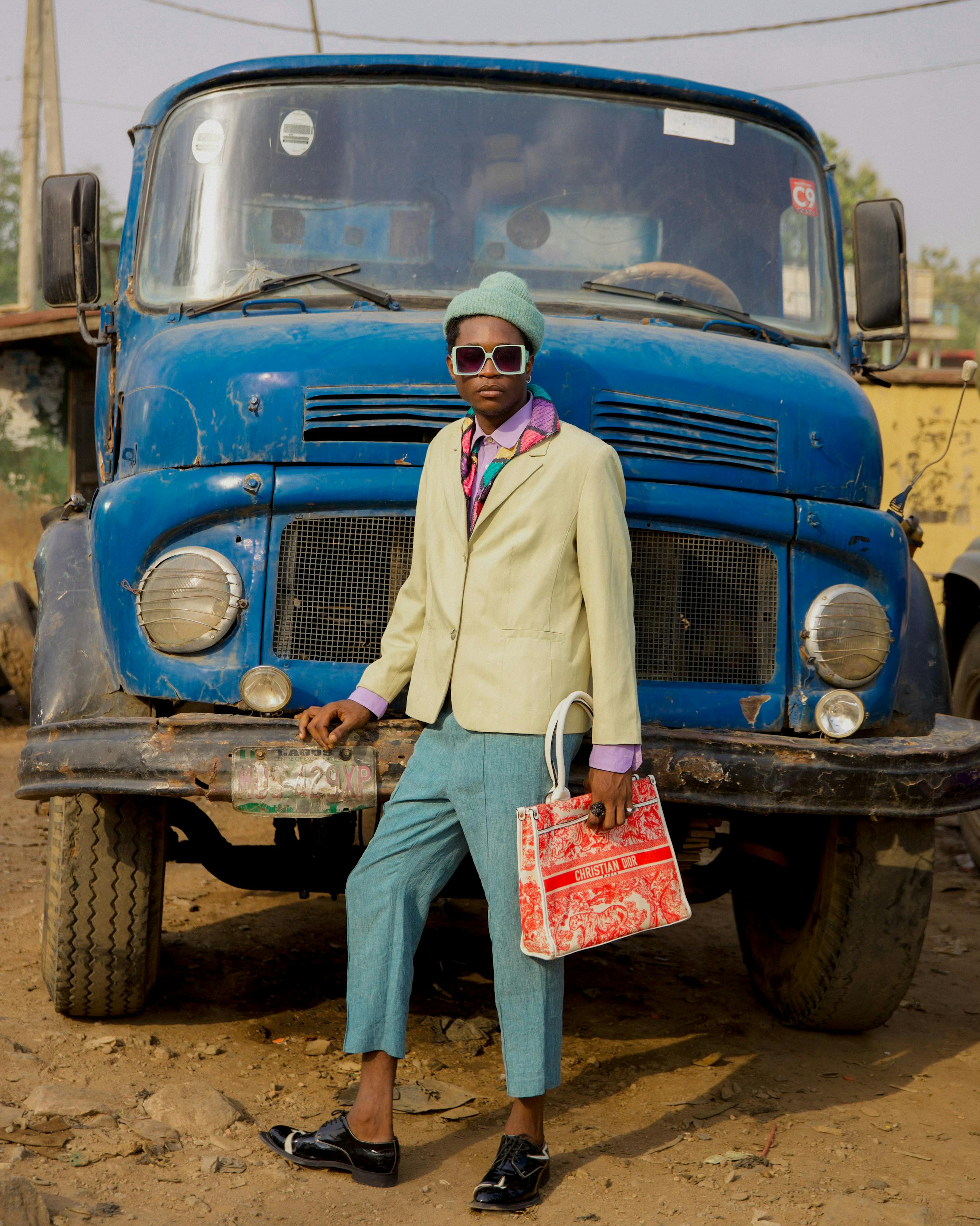 A fashionable model in colorful attire poses confidently near an old blue truck.