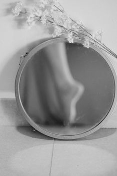 A delicate reflection of a leg in a circular mirror with floral decor.