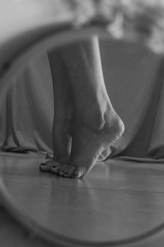 Black and white photo capturing bare feet in a mirror reflection, standing on tiptoe.