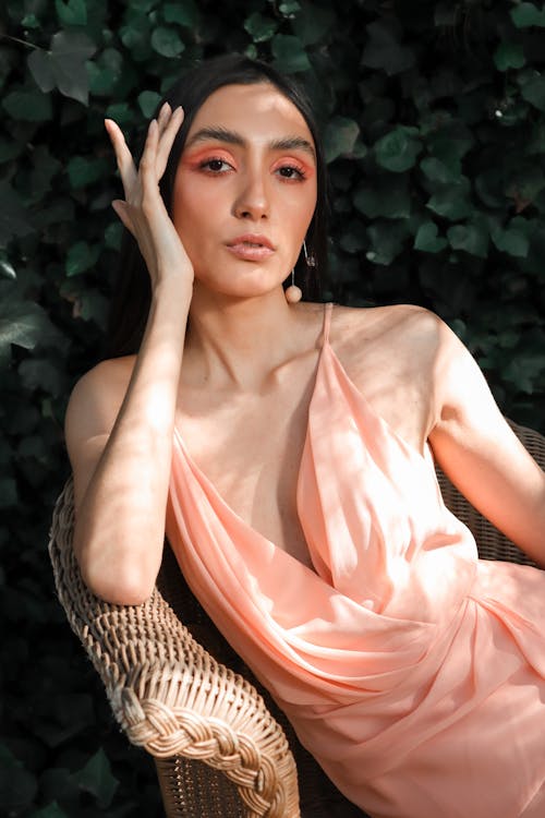 Young Woman in a Pink Dress Sitting on the Background of Green Ivy 