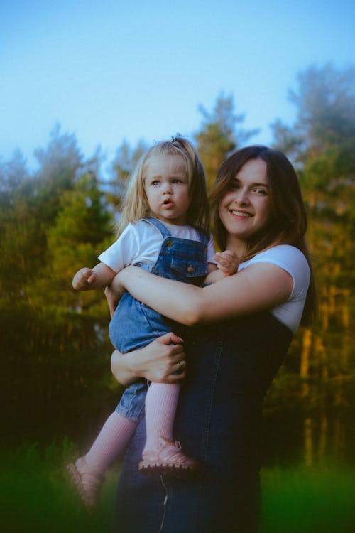 A woman holding a child in front of a forest