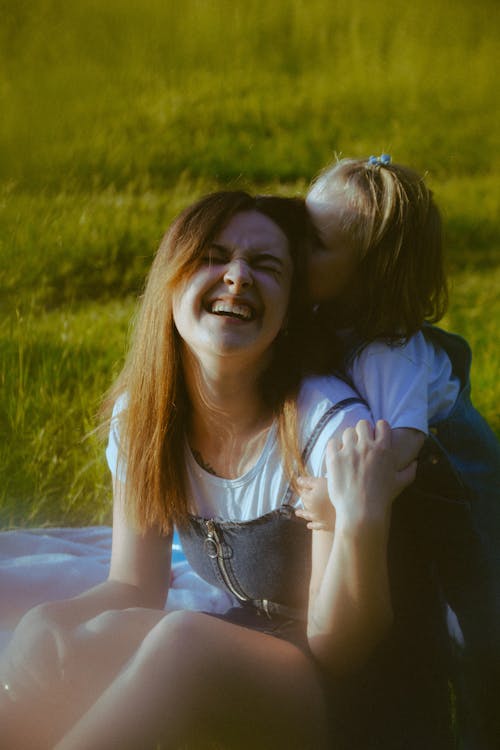 A woman and a little girl are laughing in a field