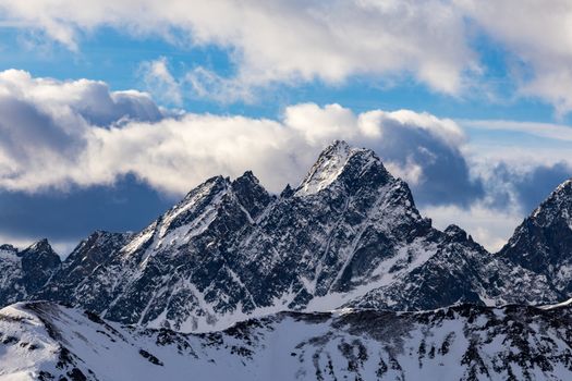 A dramatic view of snow-covered mountain peaks against a backdrop of clouds, capturing winter's beauty.