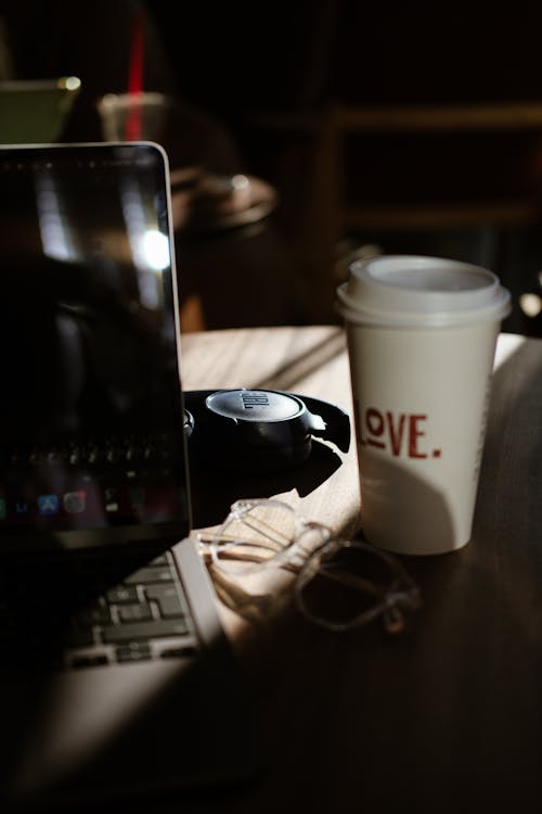 A laptop, coffee cup and earphones sit on a table