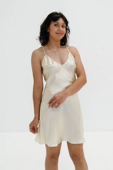 A young woman poses confidently in a silky, elegant dress with a minimalist background.