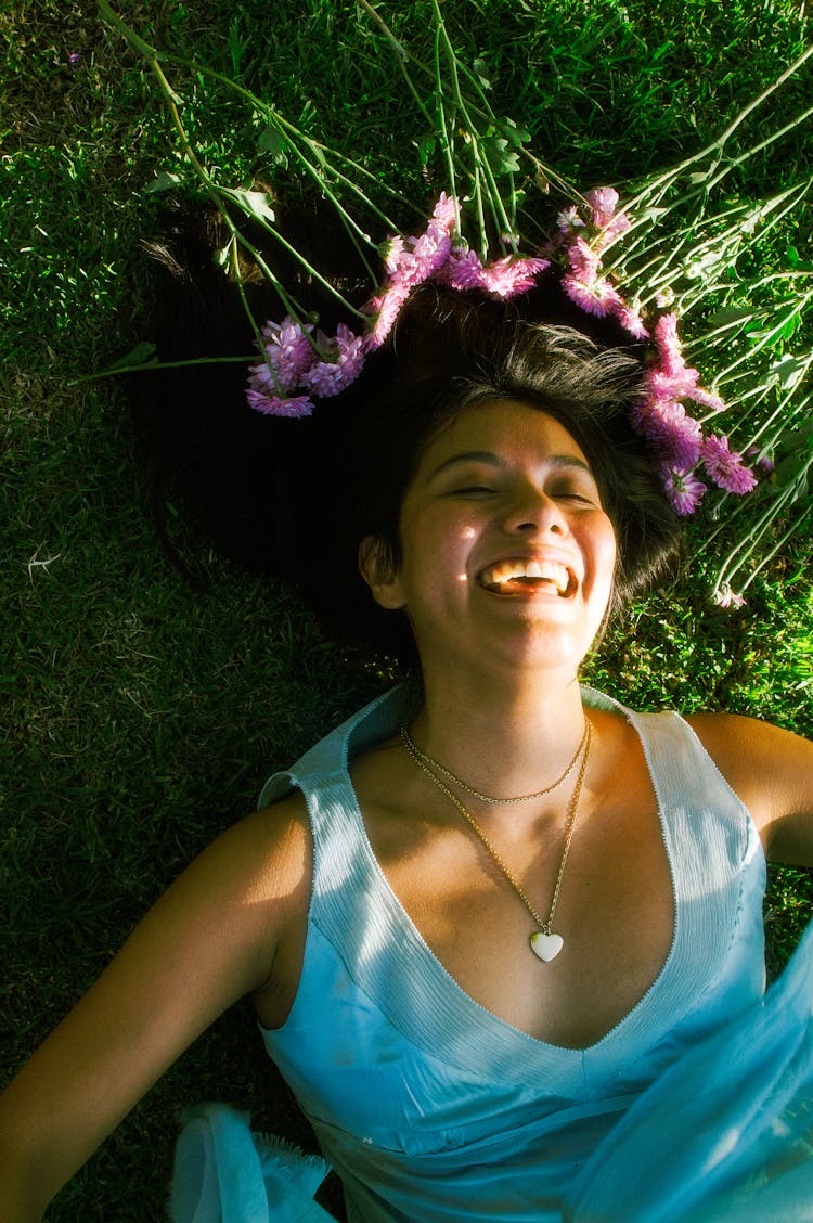 Happy Brunette Woman Lying On Grass By Pink Flowers