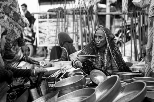 Free A monochrome image capturing an elderly Indian woman selling pots in a vibrant street market. Stock Photo