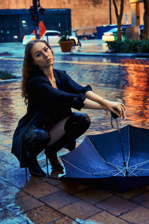 A woman kneeling in the rain holding an umbrella