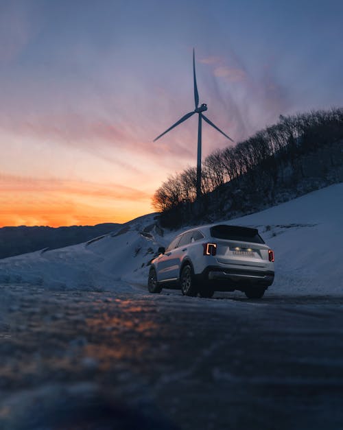 The left rear view of the Kia Sorento driving on a snow-covered road under a sunset sky.