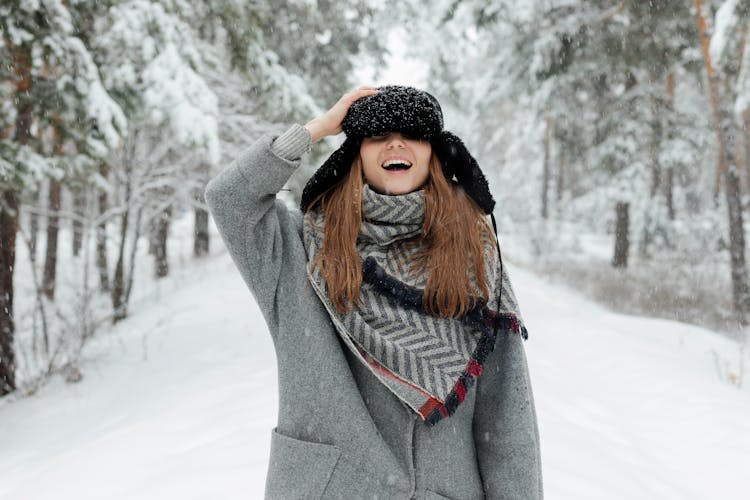 Woman In Grey Coat Holds Cap And Stands In The Middle Of Snow Covered Ground