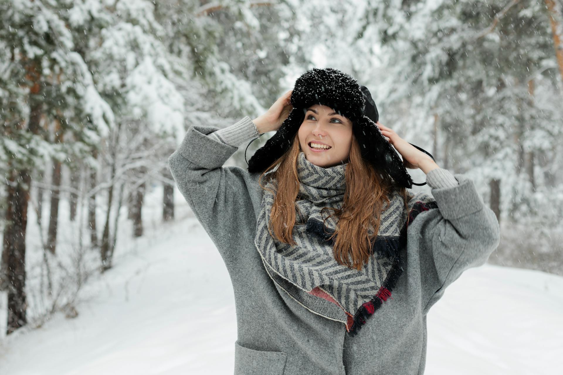 A cheerful woman in a winter coat and scarf enjoying a snowy day in a forest.