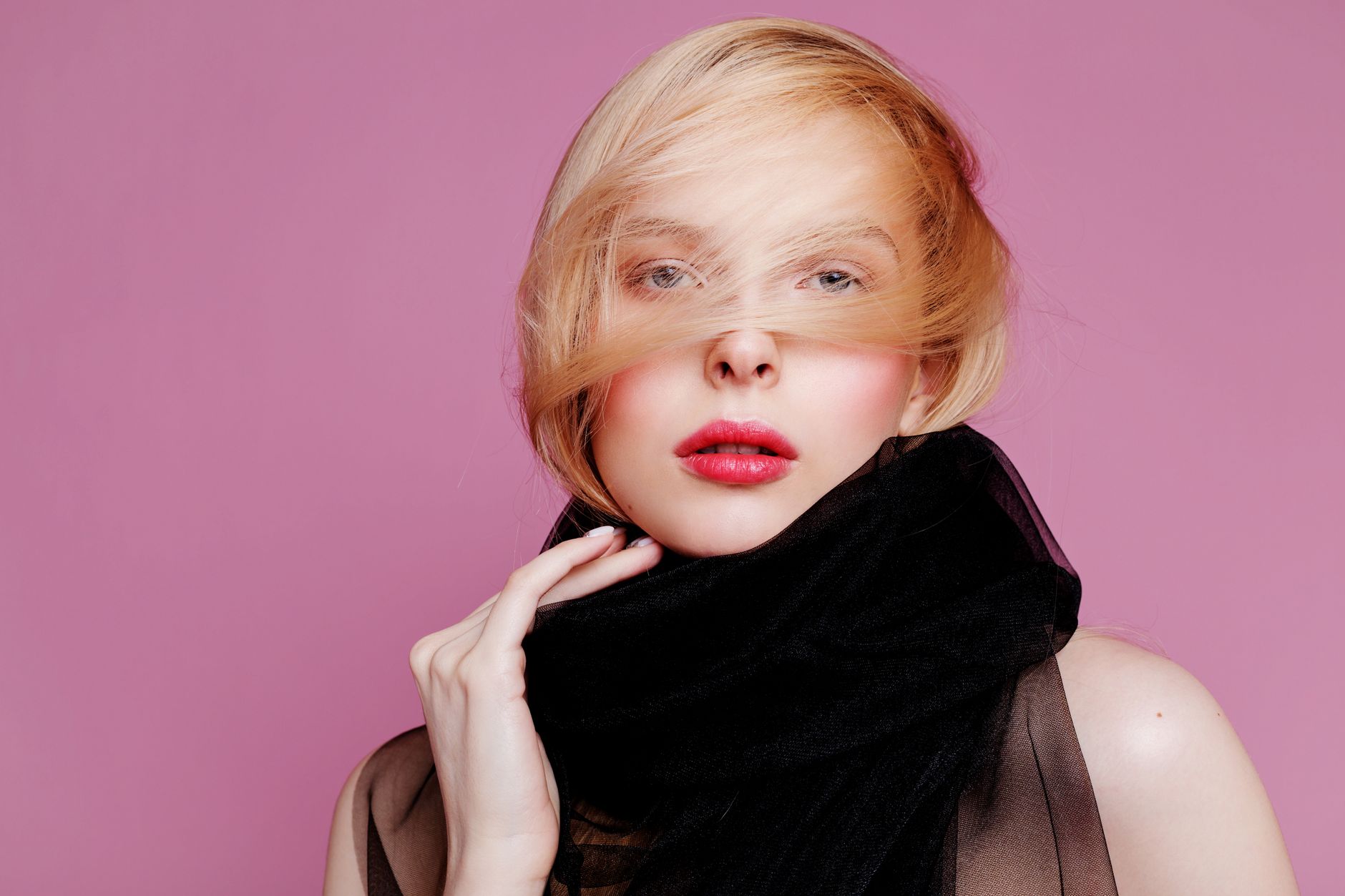 Stylish portrait of a woman wearing a black scarf with pink background, showcasing elegance.