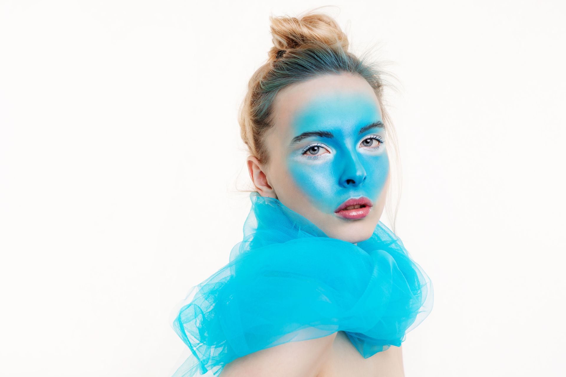 A creative portrait depicting a female model with vibrant blue face paint and an elegant expression.