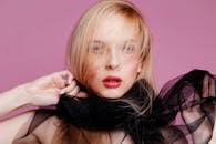 一位金发碧眼、围着纯黑围巾的女性时尚特写肖像，背景为粉色