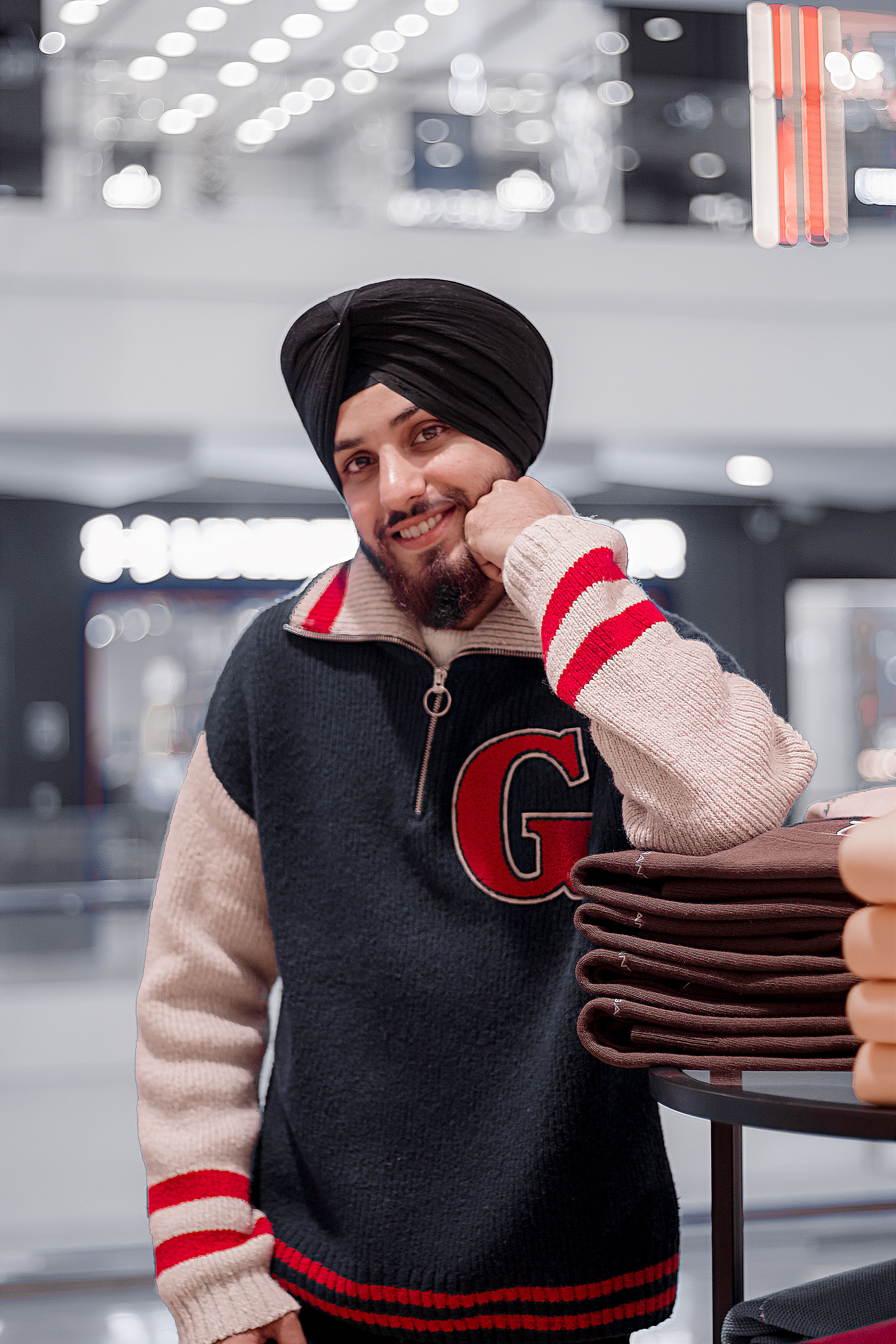 Smiling man in a sweater and turban posing indoors in a New Delhi mall.