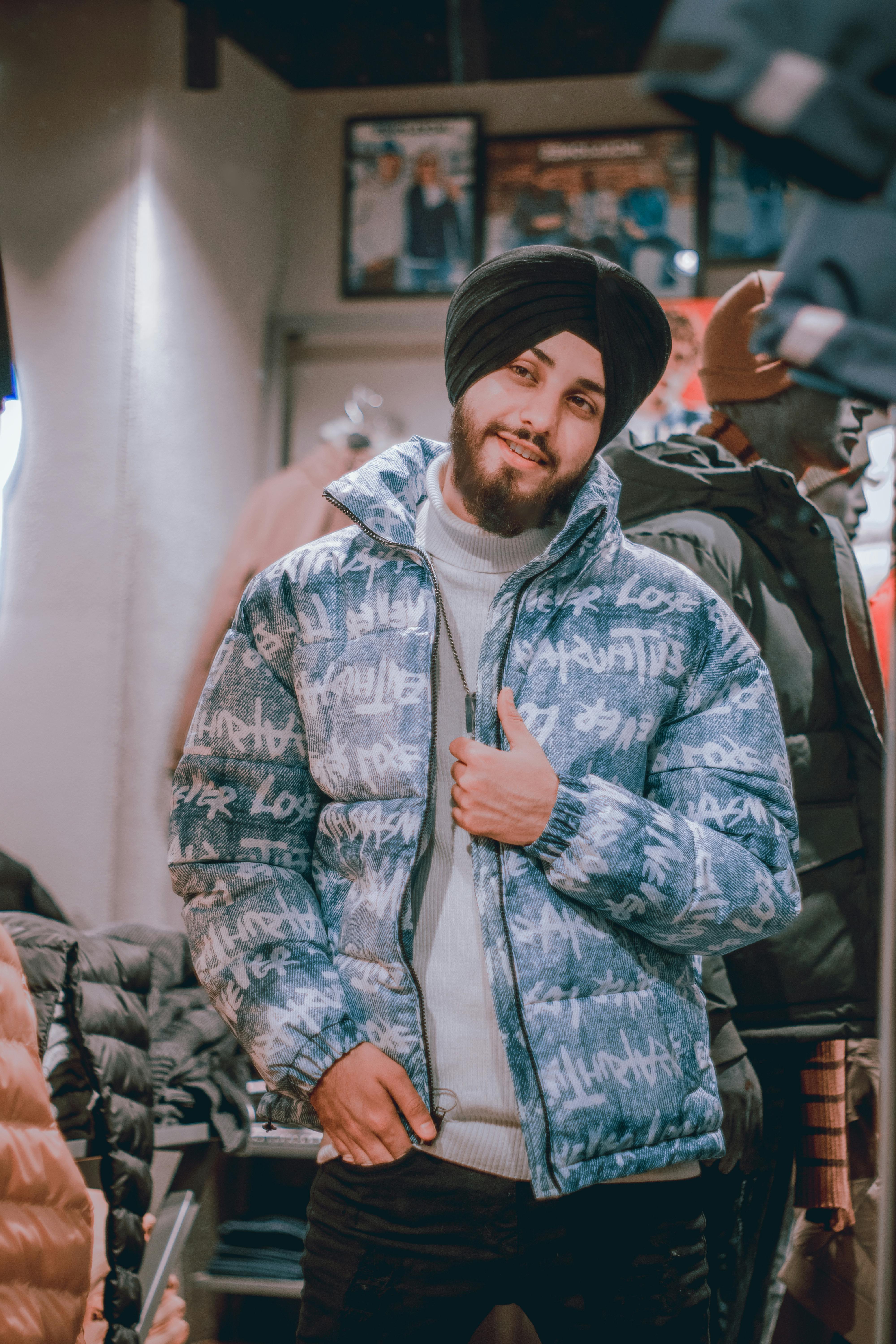 Portrait of a smiling man in a stylish winter jacket and turban, captured indoors.