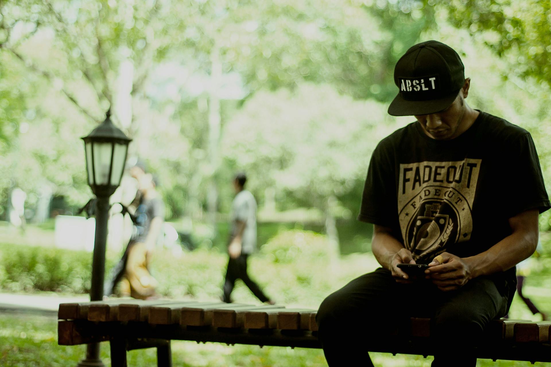 Casual outdoor scene of a young man sitting on a bench in a lush Indonesian park.