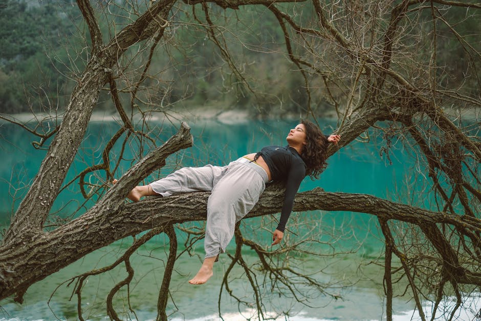 A woman laying on a tree branch near a lake