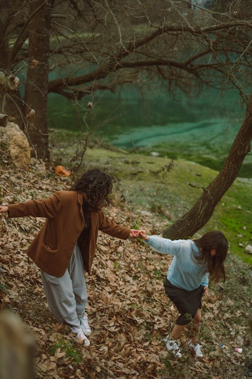 Two women are walking through the woods with a lake in the background