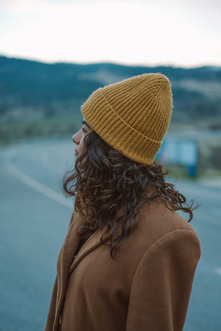 Young Woman In A Brown Coat And Yellow Hat Standing Outside 