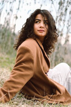 Portrait of a woman in a brown coat sitting in a natural setting. Curly-haired model looks away, capturing a serene moment.