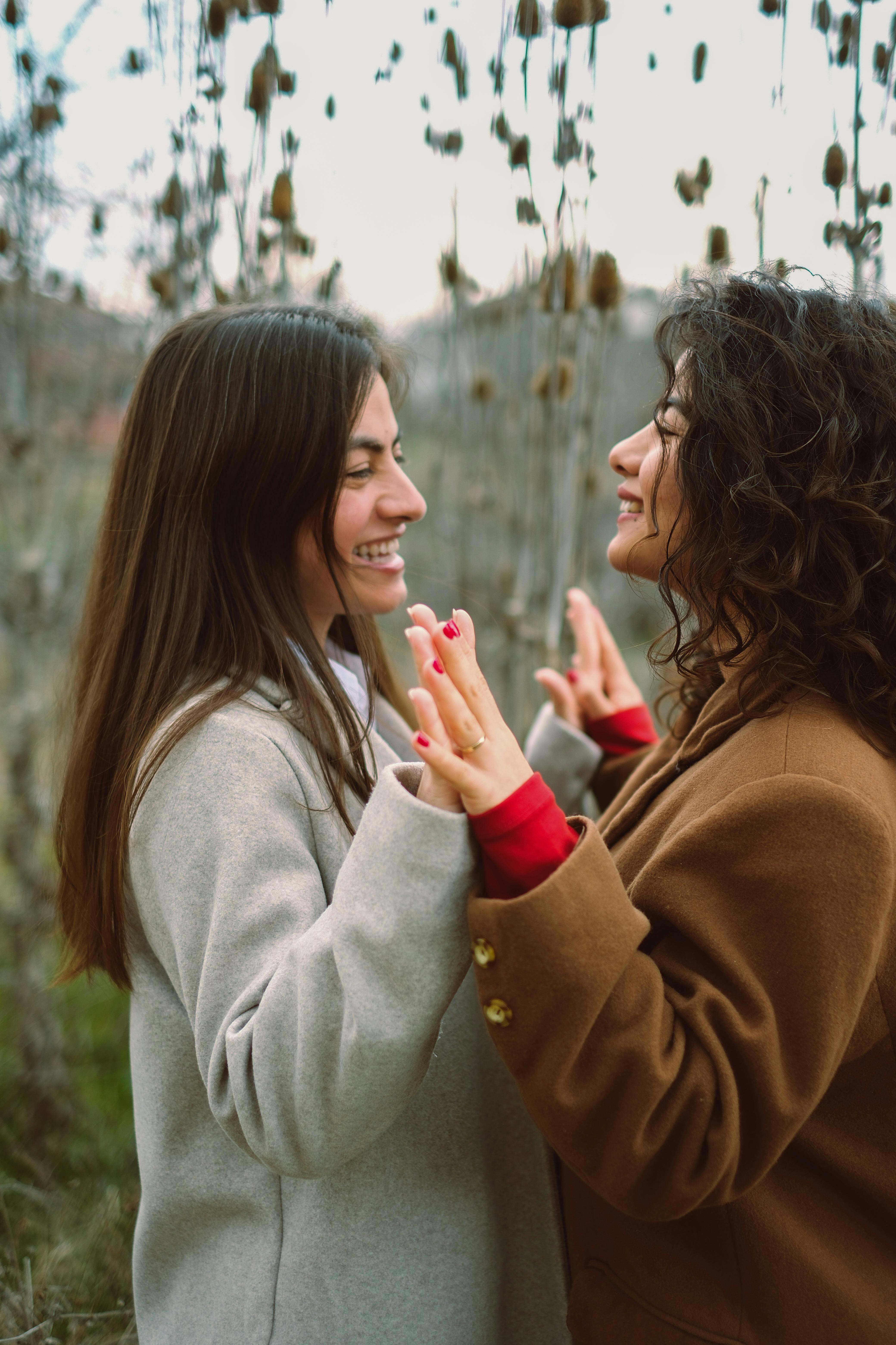 Two women in coats joyfully interact in a natural outdoor setting, showcasing friendship and happiness.