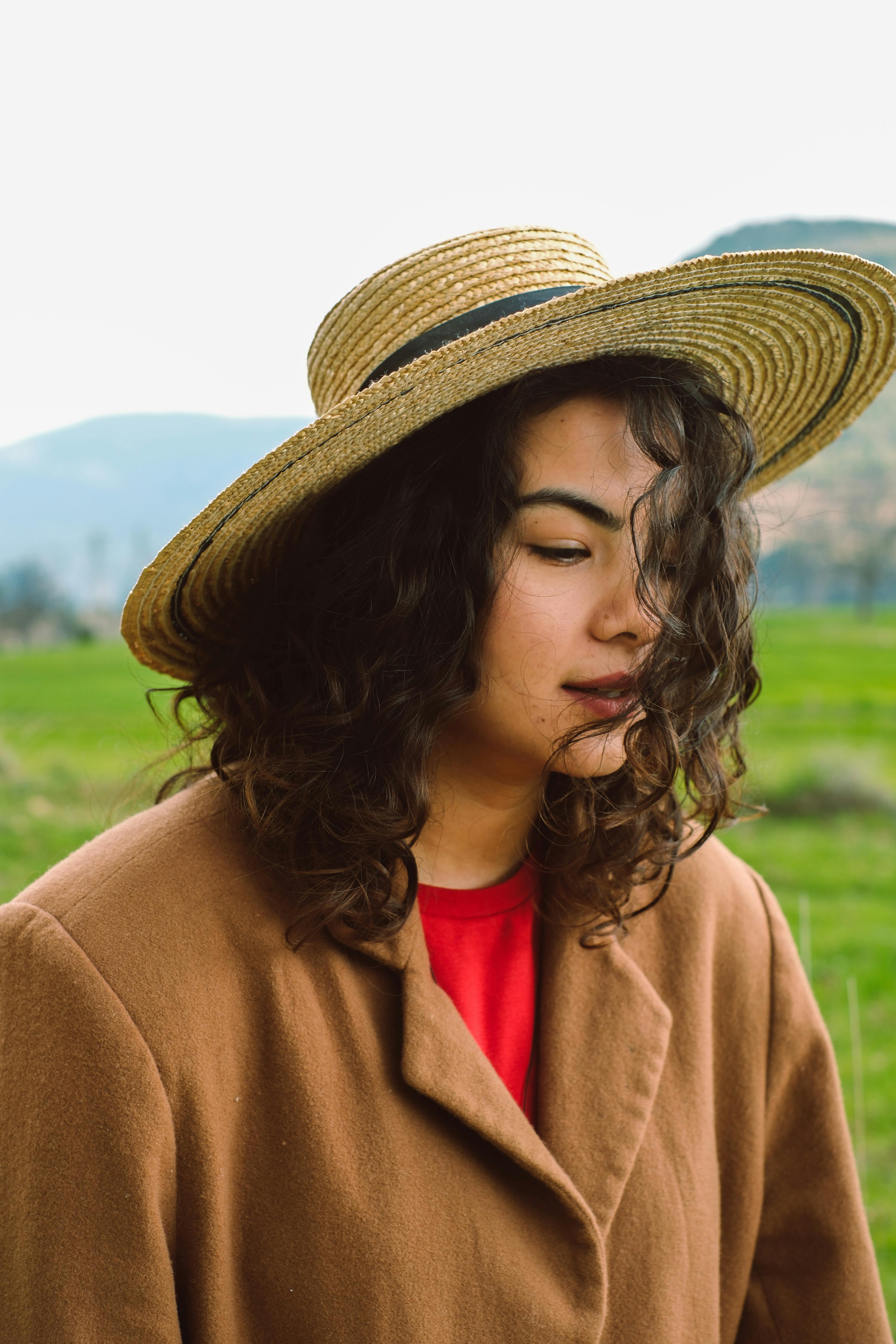 Portrait of a woman in a straw hat and coat standing in a field.