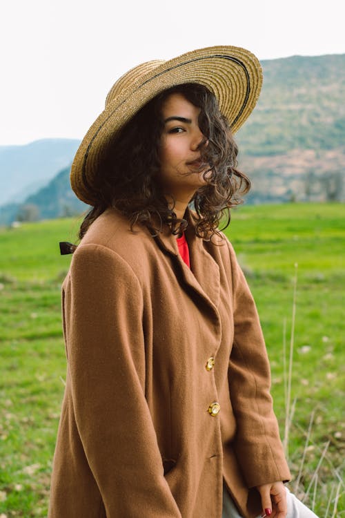 A woman in a brown coat and hat standing in a field