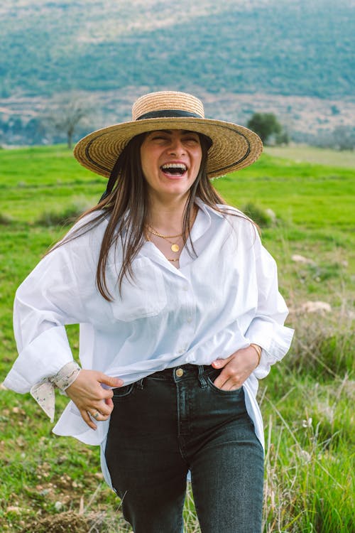 A woman in a hat and jeans smiles in a field