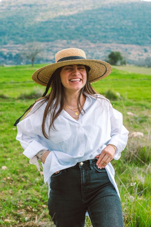 A woman in a hat and jeans smiling in a field