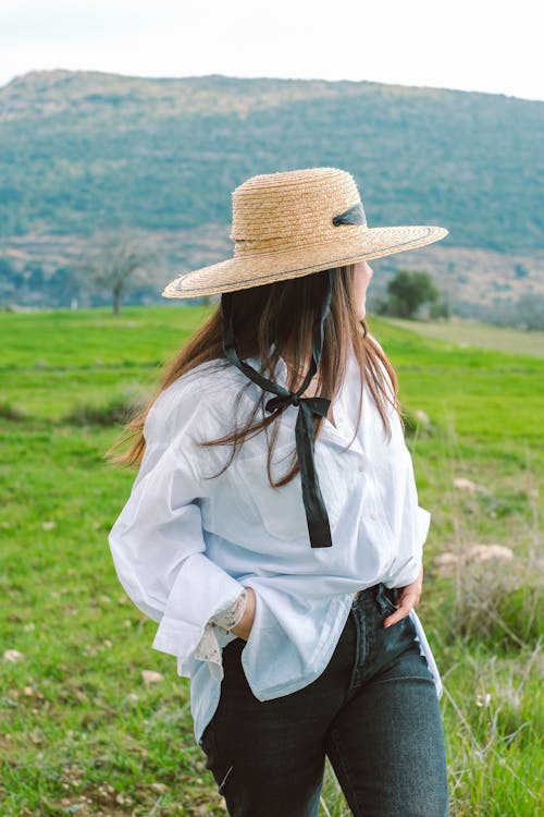 Tourist in a Straw Hat on a Meadow in the Mountains