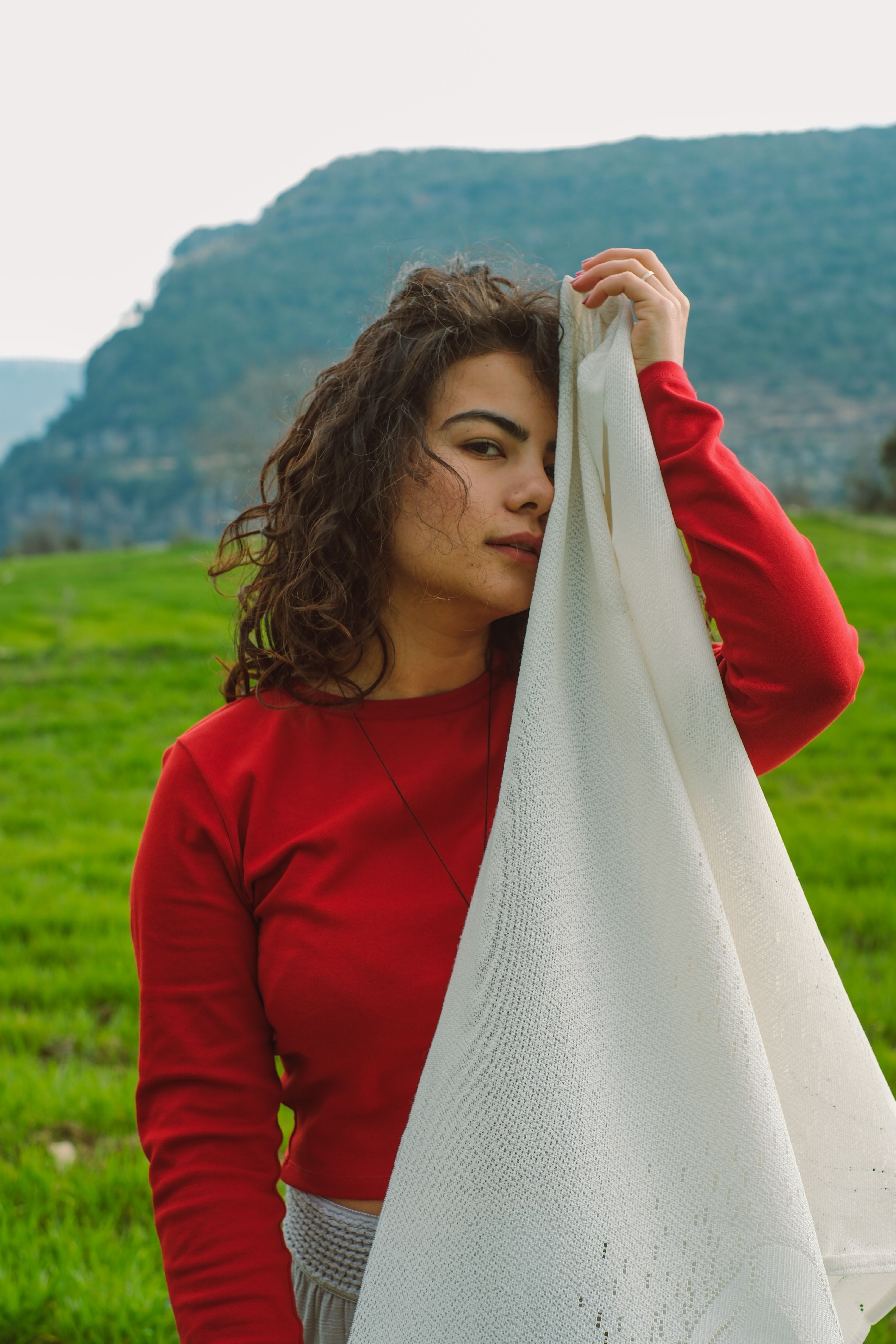 A young woman poses in a scenic outdoor setting, holding a white cloth.