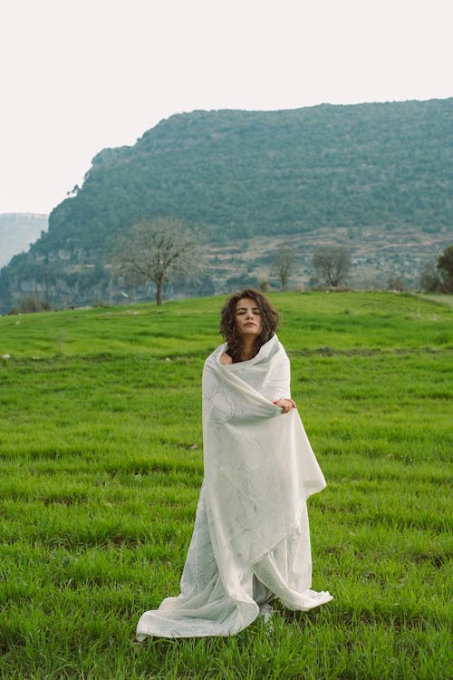 A woman in a white blanket standing in a field